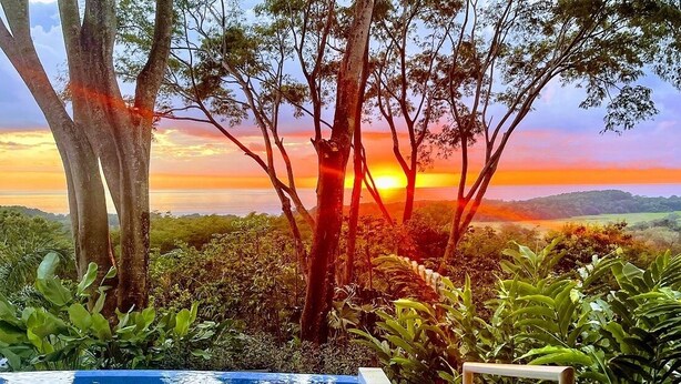 Ein Pool mit Blick auf einen Sonnenuntergang über einer Landschaft mit Bäumen und Hügeln.