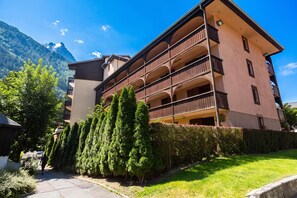 A multi-story building with balconies, surrounded by greenery and mountains.