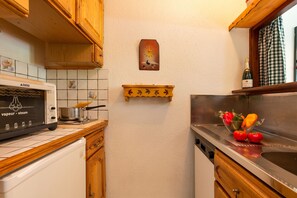 A kitchen with wooden cabinets, a microwave, a stove, a clock, and a bottle of wine on the counter.