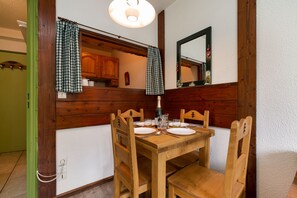 A wooden dining table with four chairs, a mirror above, and a checkered curtain.