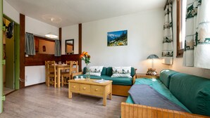 Een gezellige woonkamer met een houten vloer, een groene bank, een houten salontafel en een eethoek met een houten tafel en stoelen.
