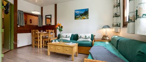Ein gemütliches Wohnzimmer mit Holzboden, einer grünen Couch, einem Holztisch und einer Essecke mit Tisch und Stühlen.