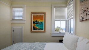 Un dormitorio con cama, ventana con persianas, puerta y un cartel enmarcado en la pared.