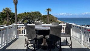 Una terraza con una mesa redonda y cuatro sillas, con vista a una zona costera con palmeras y vistas al océano.
