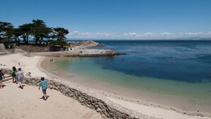 Una playa con agua cristalina, un promontorio rocoso y algunas personas caminando por la orilla.
