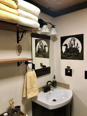 A bathroom with a white sink, black faucet, and a towel rack with folded towels. There are two wall-mounted lights and two framed pictures of birds. - Walkable private suite in the heart of the village of Clinton, NY. 13323 (Clinton)