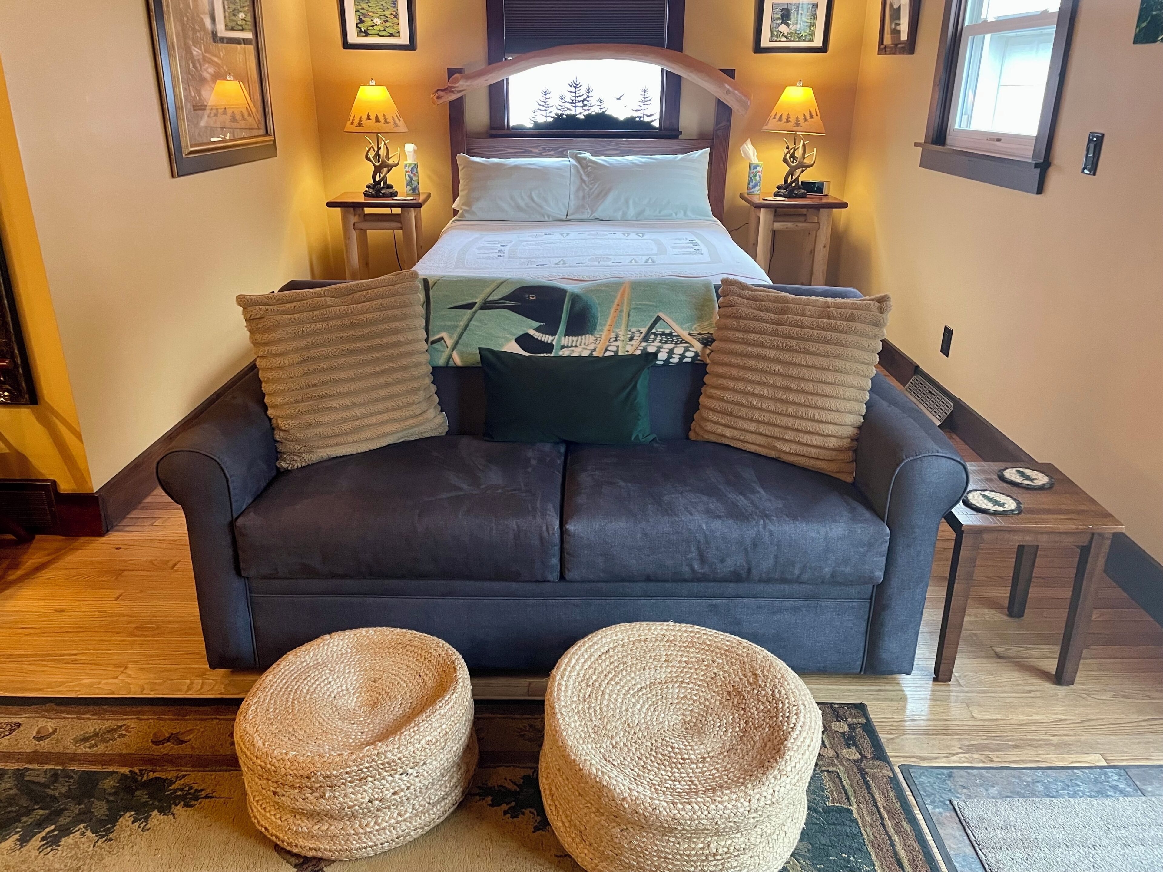 Une chambre à coucher comprenant un lit, deux tables de chevet, deux lampes, une fenêtre et deux poufs en osier.