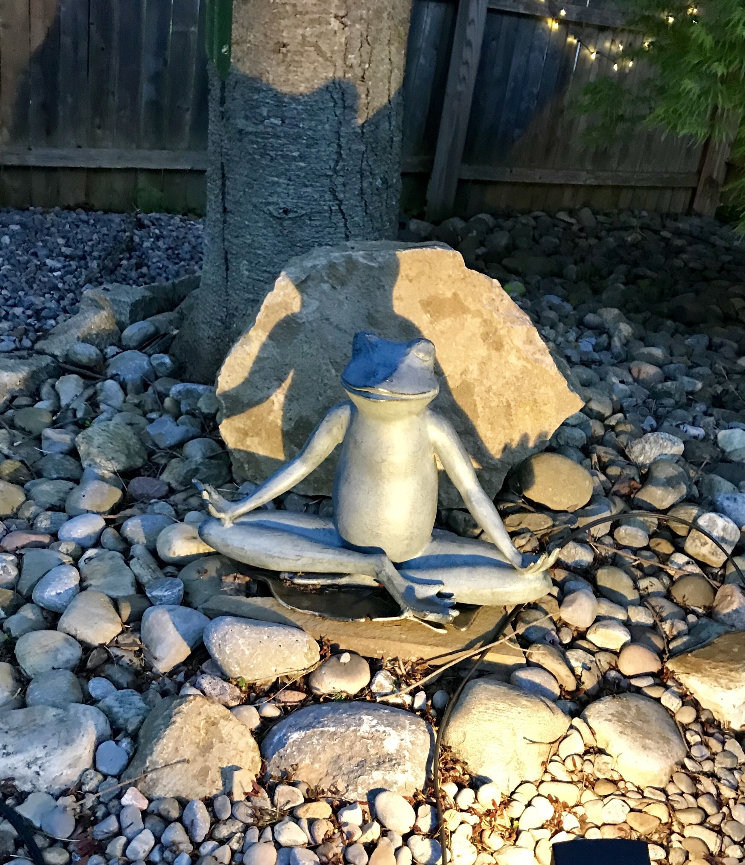 Une sculpture représentant une figure en position méditative, placée sur un piédestal en pierre et entourée de petits galets.