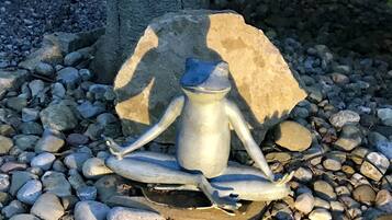 Une sculpture représentant une figure en position méditative, placée sur un piédestal en pierre et entourée de petits galets.