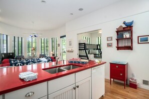 Une cuisine avec un plan de travail rouge, des placards blancs et un évier. On y trouve une table de chevet rouge avec des tiroirs et une petite poubelle rouge.