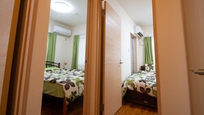 A bedroom with two beds, green curtains, and an air conditioning unit on the wall. - Pine House in ISHIGAKI (Ishigaki)