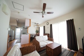 A living room with a sofa, a coffee table, and a ceiling fan. There is a kitchen area visible in the background. - Pine House in ISHIGAKI (Ishigaki)