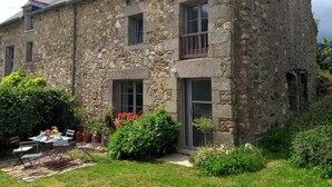 A stone building with multiple windows and a balcony. There is a small garden with potted plants and flowers. - Charming stone cottage completely renovated in 2019 (Pleslin-Trigavou)