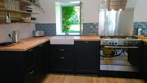 A modern kitchen with dark cabinets, a stainless steel stove, and a window with a view of greenery. - Charming stone cottage completely renovated in 2019 (Pleslin-Trigavou)
