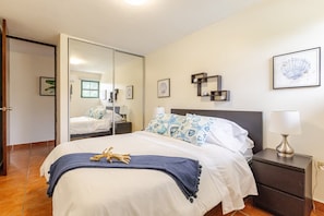 A hotel room with a bed, a nightstand, a mirror, and artwork on the walls.