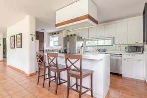 A modern kitchen with white cabinets, a central island with bar stools, and a built-in microwave. - Beautiful Getaway Home | Private Pool | 4BD (Luquillo)