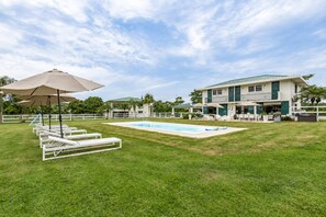 Zona de piscina amb gandules i ombrelles, un edifici amb balcó i una propietat tancada per una tanca.