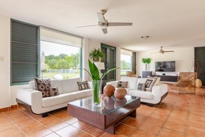 A modern living room with a glass coffee table, white sofas, and a TV. - Beautiful Getaway Home | Private Pool | 4BD (Luquillo)