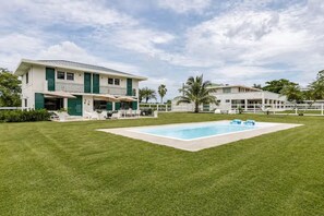 A two-story house with a swimming pool, green lawn, and palm trees. - Beautiful Getaway Home | Private Pool | 4BD (Luquillo)