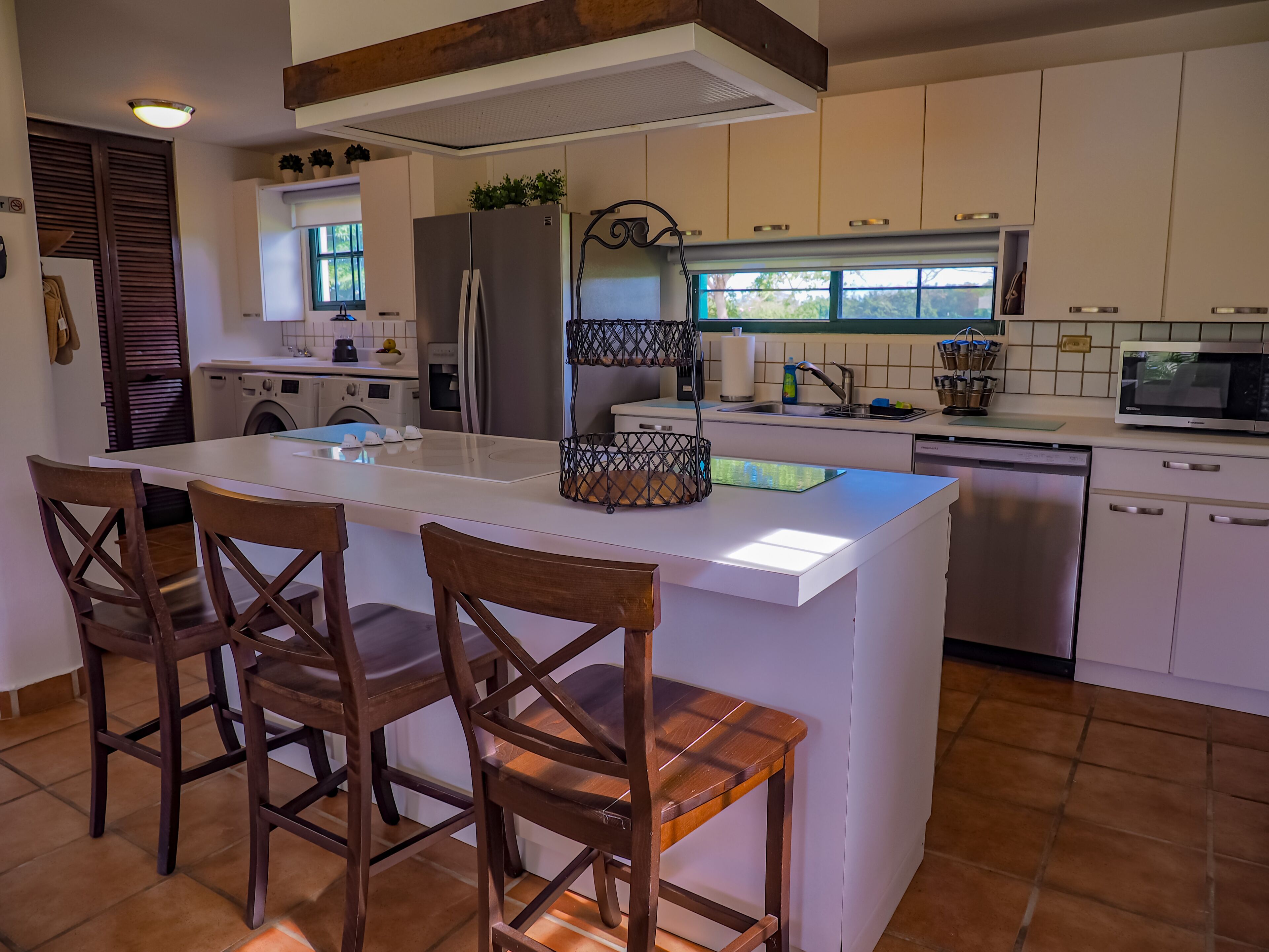 A modern kitchen with a central island, bar stools, a built-in oven, a microwave, and a dishwasher.
