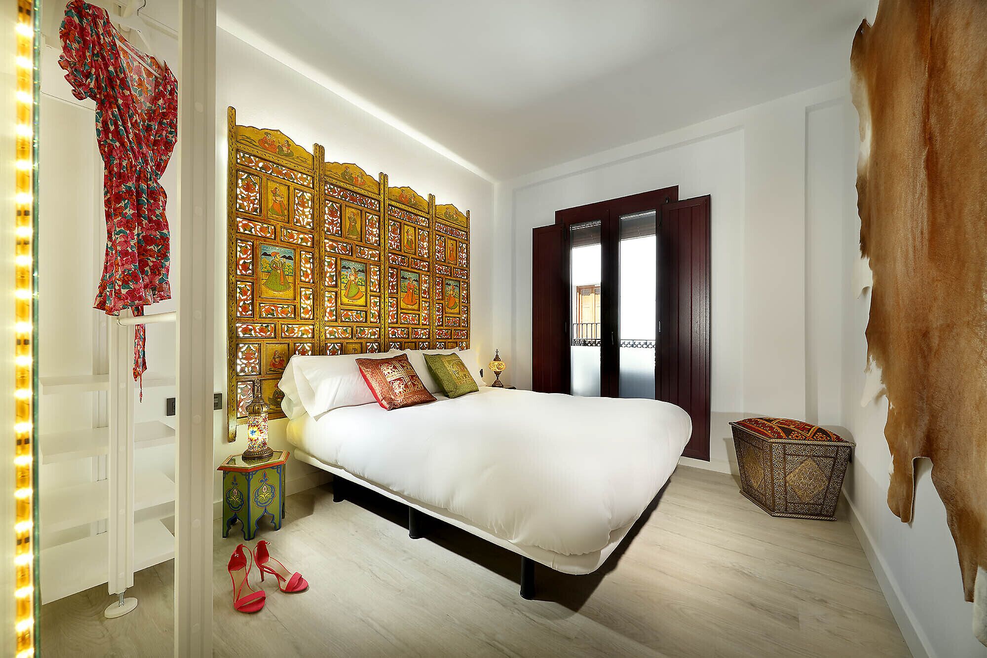 Un dormitorio con cama, un adorno en la pared, una puerta y una mesita.