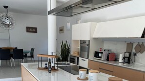 Een moderne keuken met een centraal eiland, een eethoek met een groene stoel, en een keukenblad met apparatuur.