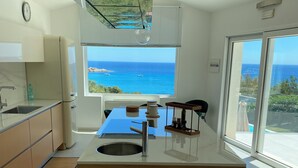 Een moderne keuken met een centraal eiland, een inbouwoven en uitzicht op de zee.