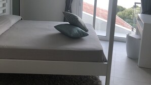 Een moderne slaapkamer met een bed, een klein nachtkastje, een raam met gordijnen en uitzicht op de omgeving.