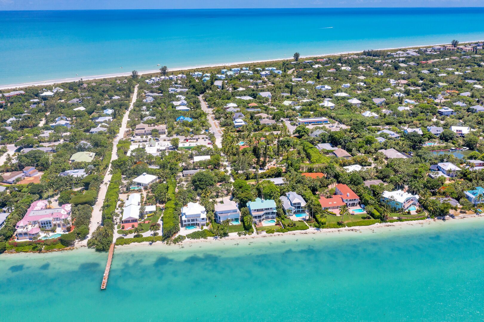 Vista aérea de una zona residencial costera con casas, una playa y un muelle.