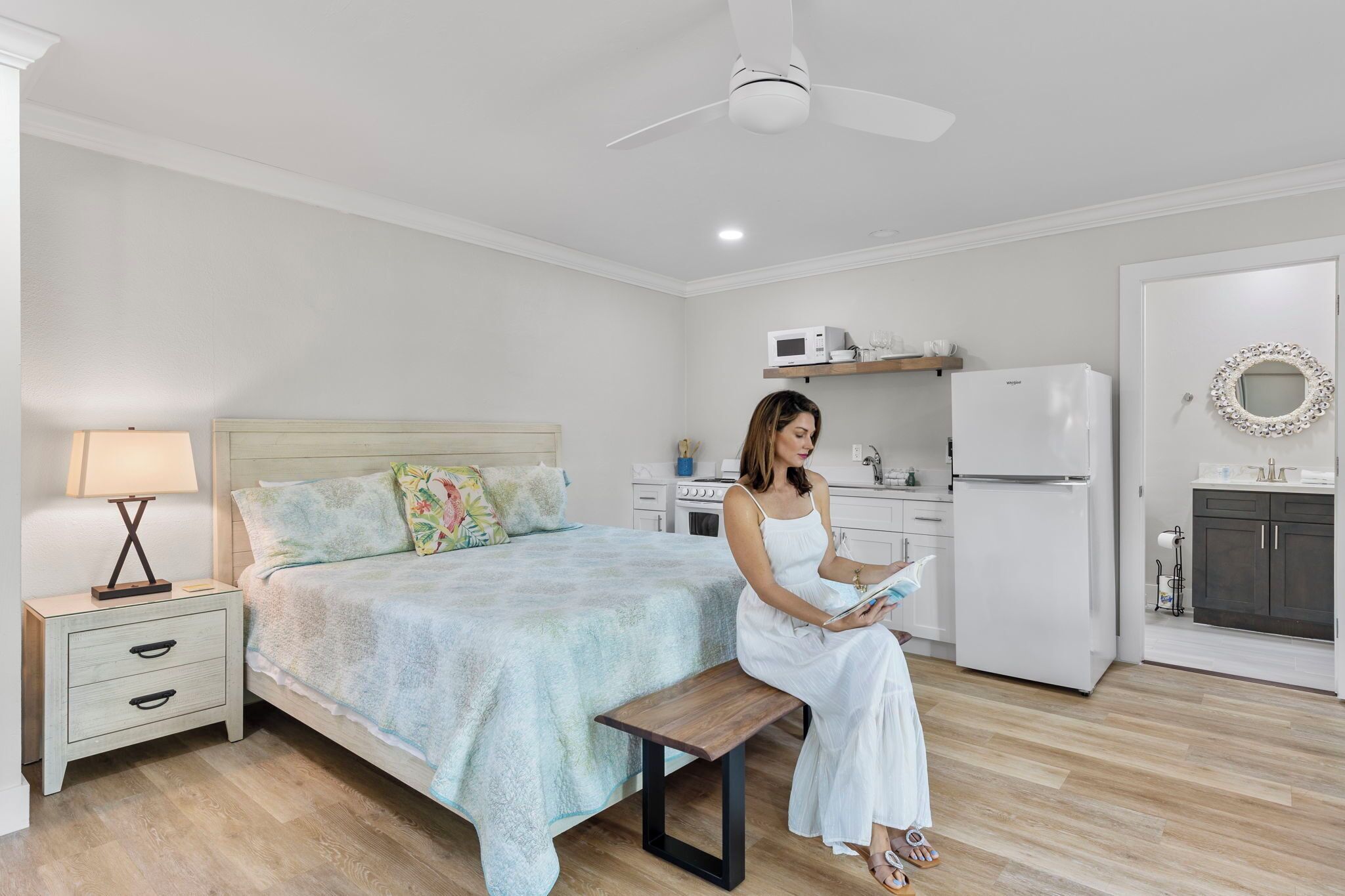 A bedroom with a bed, bedside table, lamp, and a person reading a book.