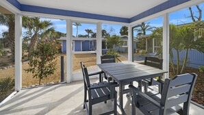 A covered patio area with a table and chairs, large windows, and a view of the surrounding landscape. - Gorgeous Newly Renovated Coastal Cottage "Egret" Minutes to the beach and free bikes!! JULY SAVINGS! (Sanibel)