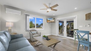 A modern living room with a grey sofa, a wooden coffee table, and a ceiling fan. - Gorgeous Newly Renovated Coastal Cottage "Egret" Minutes to the beach and free bikes!! JULY SAVINGS! (Sanibel)