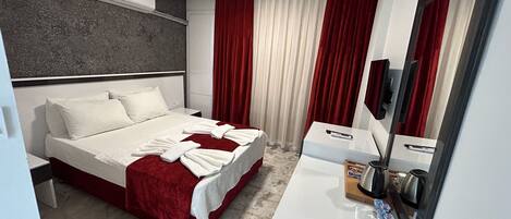 A hotel room with a bed, a bedside table, a mirror, and a window with curtains.