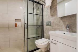 A modern bathroom with a glass shower enclosure, a white toilet, and a white sink with a mirror above. - Bellissima Hotel (Manavgat)