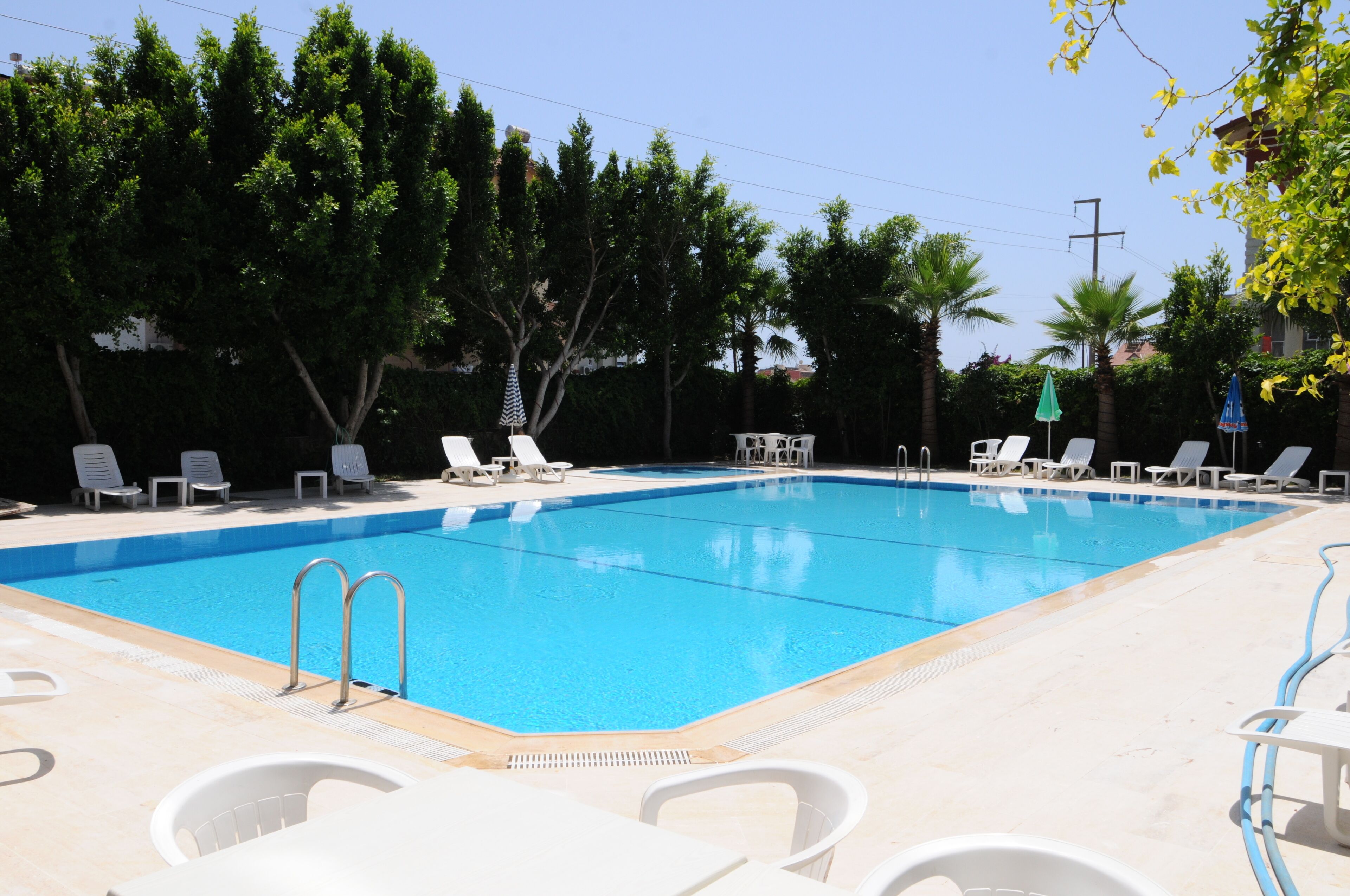 A rectangular swimming pool with clear blue water, surrounded by white lounge chairs and umbrellas.
