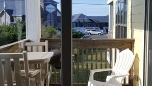 Un balcón con mesa y sillas, una silla de plástico blanco y vista a un edificio con un cartel.