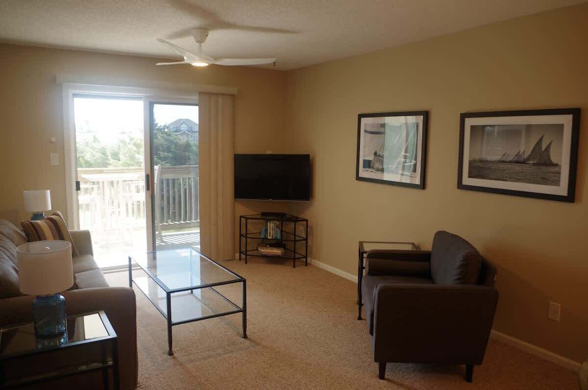 A living room with a TV, two framed pictures, a sofa, a coffee table, and a balcony door.