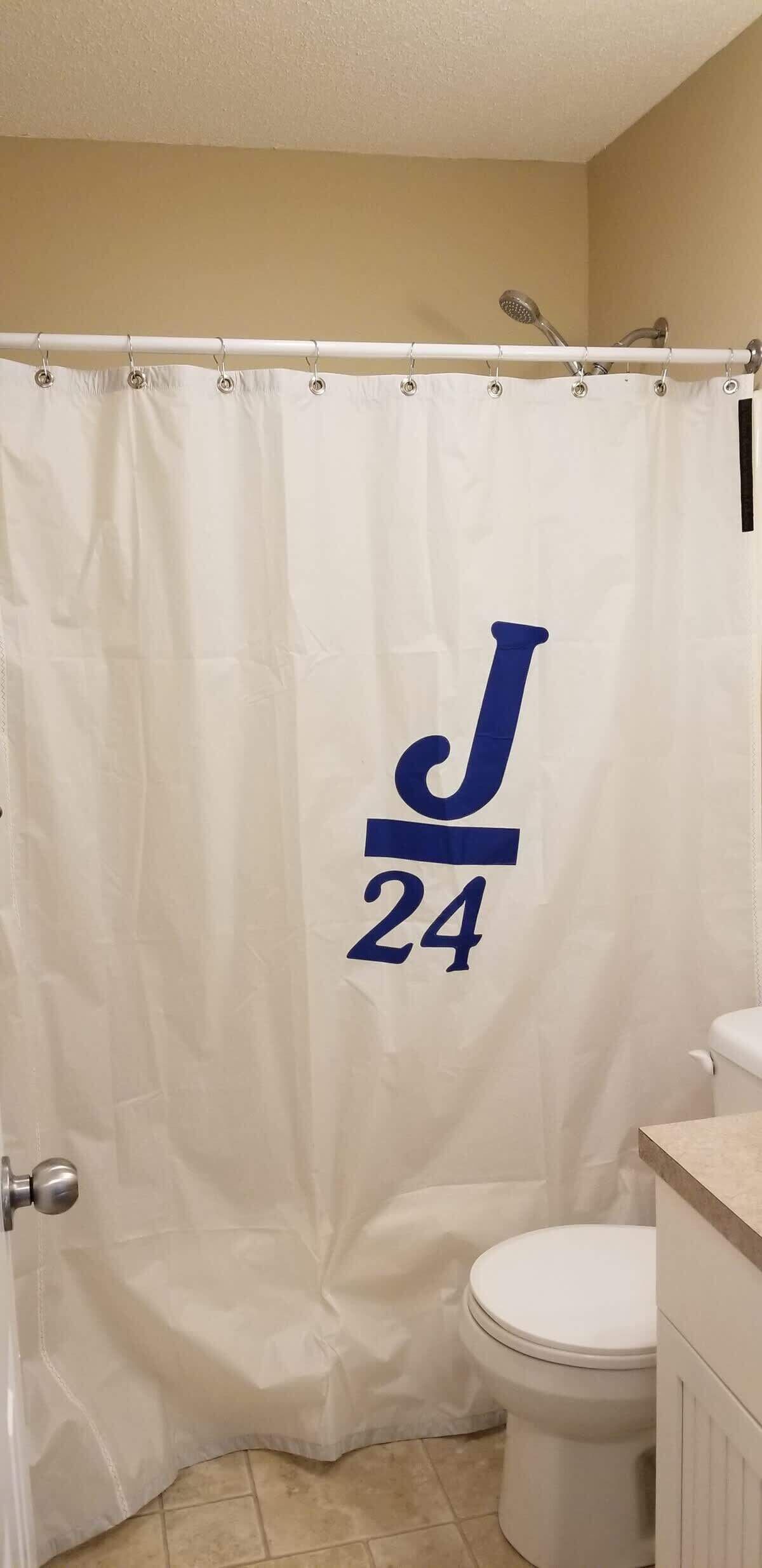 A bathroom with a white shower curtain featuring a large 'J' and the number '24' in blue.