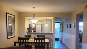 Una sala de estar con sofá, una mesa de comedor con sillas, una cocina al fondo y un pasillo que lleva a otra habitación.