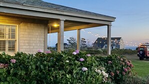 A house with a covered porch, string lights, and a vehicle in the background. - Have it all! The perfect Nantucket getaway for stunning ocean views and beaches! (Nantucket)