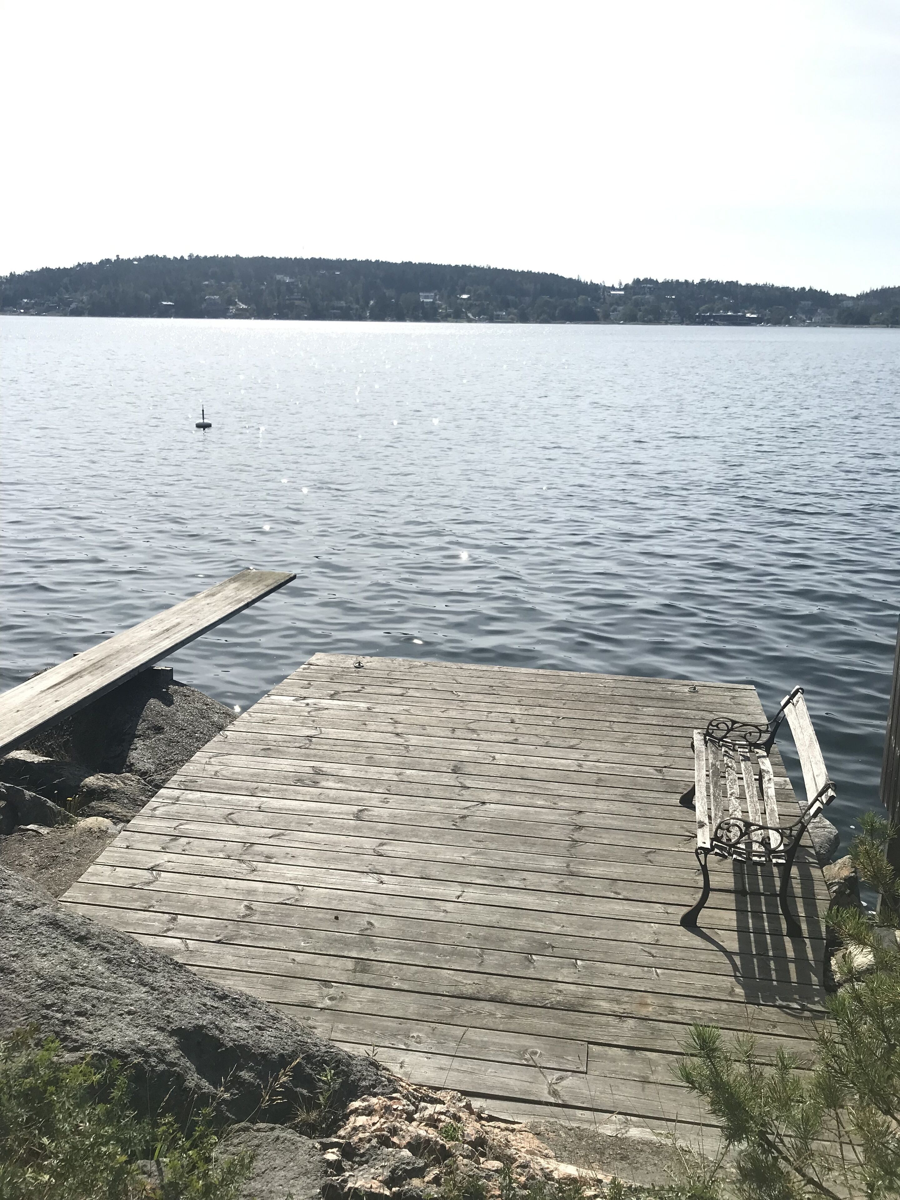 Un muelle de madera que se adentra en aguas tranquilas, con un banco y una boya.