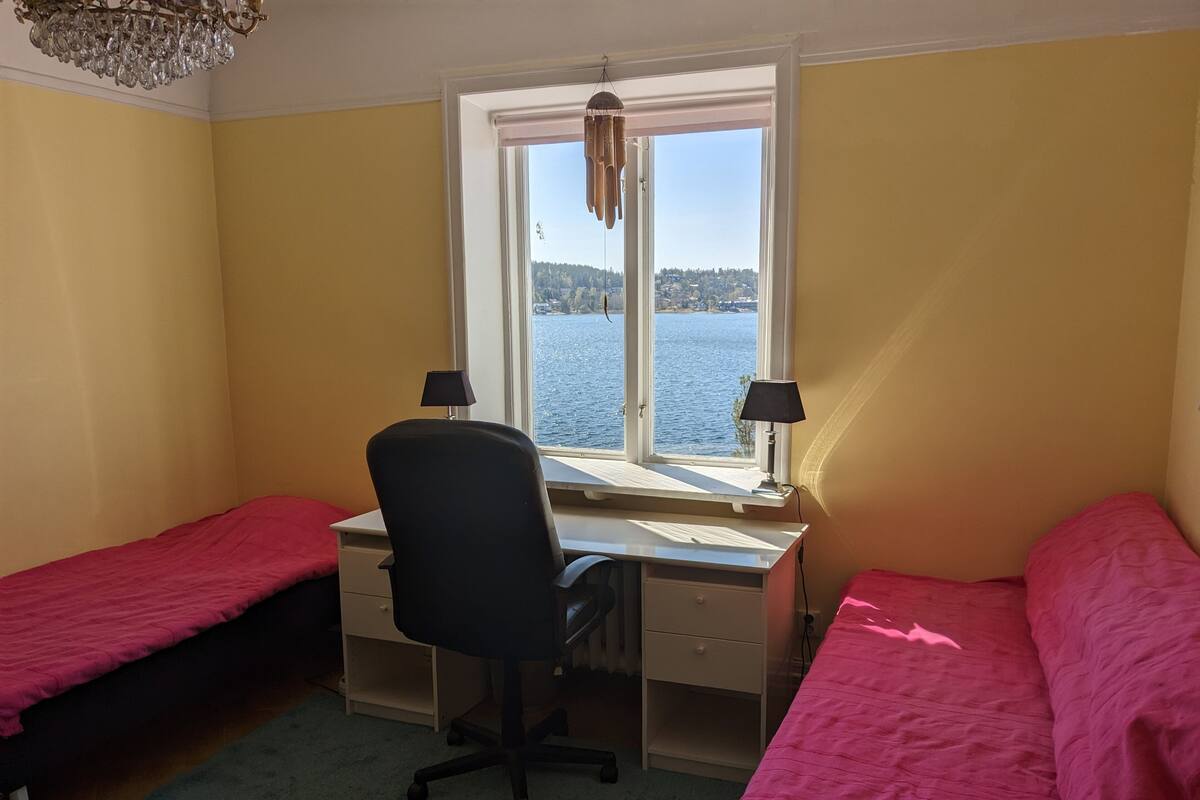 Un dormitorio con dos camas individuales, un escritorio con silla y ventana con vista a un cuerpo de agua.