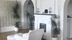 Een ruime woonkamer met een witte bank, een open haard en potplanten.