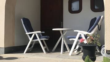 An outdoor seating area with two white tables and chairs, a potted plant, and a door.
