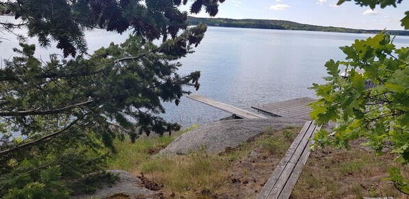 Un muelle de madera se extiende sobre un lago tranquilo, rodeado de árboles y terreno rocoso.