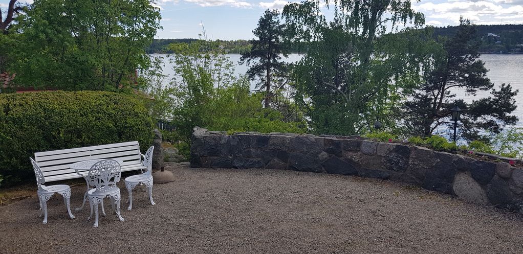 A bench with two chairs, a stone wall, and a view of a lake.