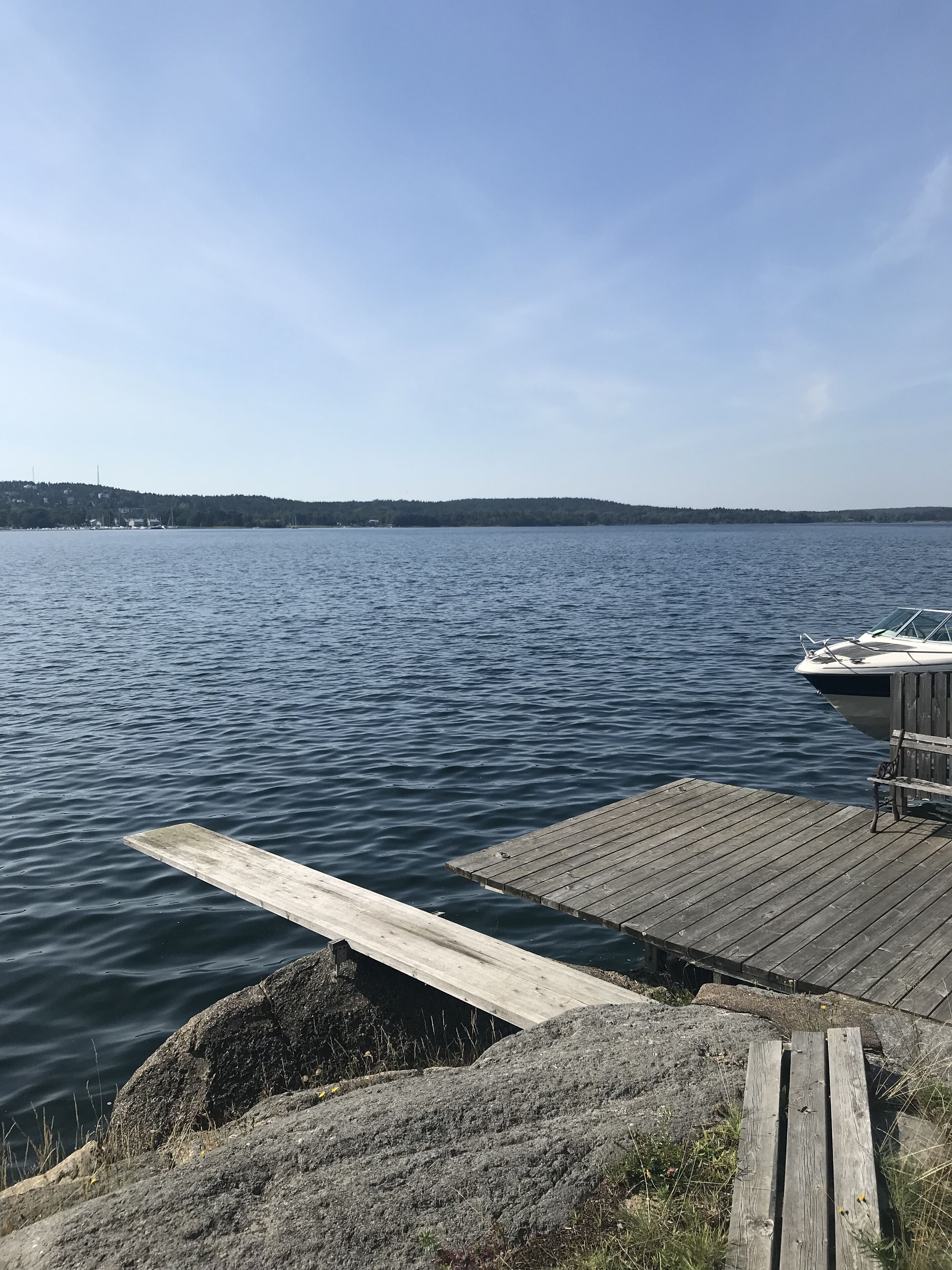En träbrygga som sträcker sig ut i stilla vatten, med en båt förtöjd på höger sida.