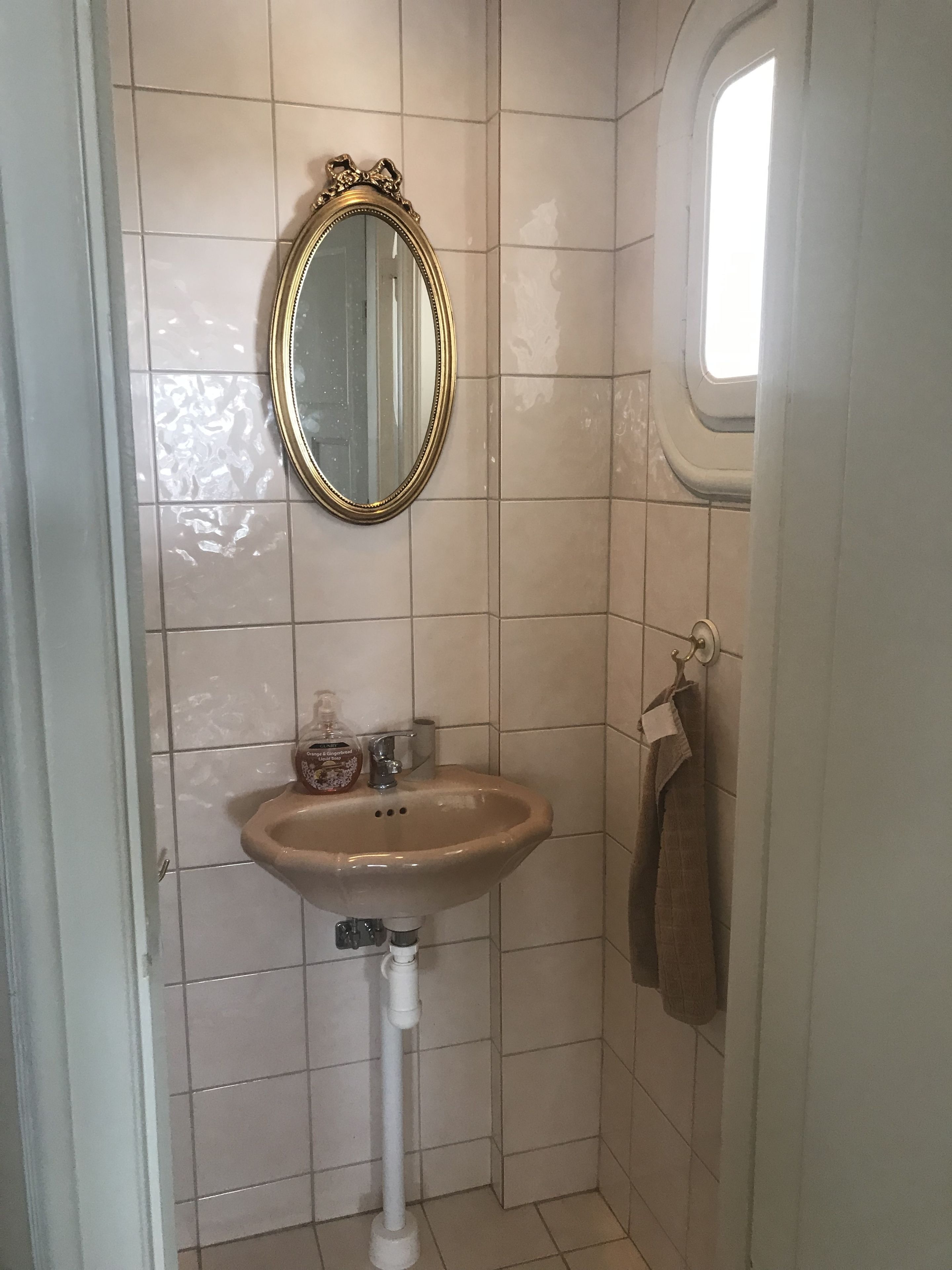 Une salle de bain avec un lavabo beige, un miroir doté d’un cadre orné et une fenêtre.