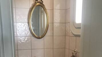 Une salle de bain avec un lavabo beige, un miroir doté d’un cadre orné et une fenêtre.