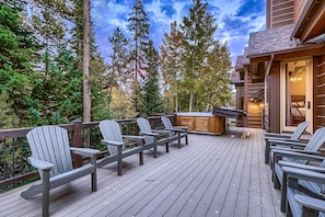 A deck with Adirondack chairs, a hot tub, and a wooden deck railing.